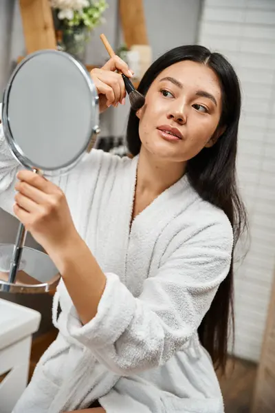 Brunette and young asian woman with blemishes applying face powder and looking at mirror, acne — Stock Photo