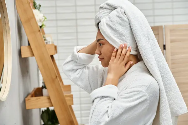 Side view of young asian woman with towel on head and acne prone skin looking at bathroom mirror — Stock Photo