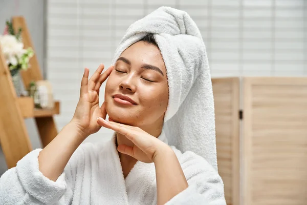 Souriant asiatique femme avec acné et serviette blanche sur la tête debout avec les yeux fermés dans la salle de bain — Photo de stock