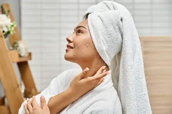 Задоволена молода азіатська жінка з акне схильною шкірою з білим рушником на голові позує у ванній — стокове фото