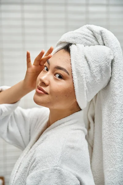 Giovane donna asiatica con acne pelle incline con asciugamano sulla testa in posa in bagno a casa, verticale — Foto stock