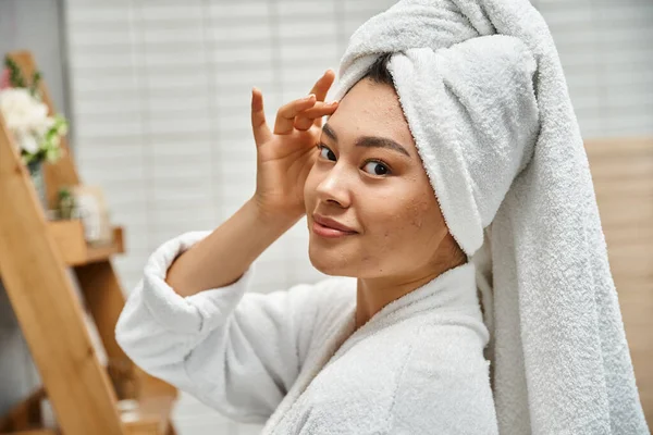 Jeune femme asiatique avec la peau sujette à l'acné avec serviette sur la tête posant dans la salle de bain à la maison, portrait — Photo de stock