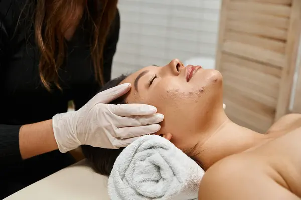 Massage facial pour peau sujette à l'acné, masseuse en gants de latex et cliente asiatique aux yeux fermés — Photo de stock
