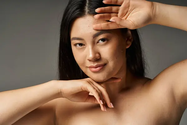 Jeune femme asiatique avec la peau sujette à l'acné et les épaules nues en regardant la caméra sur fond gris — Photo de stock