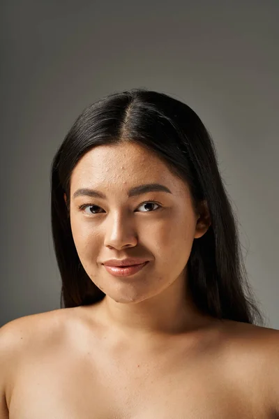 Happy young asian woman with skin issues and bare shoulders looking at camera on grey background — Stock Photo