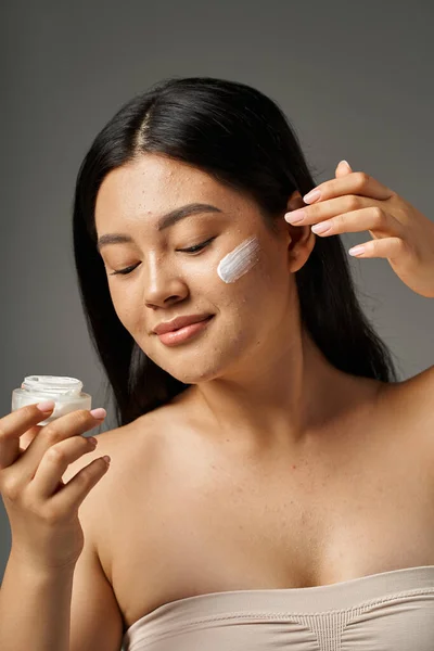 Young asian woman with brunette hair and acne prone skin looking at mirror in bathroom, banner — Stock Photo