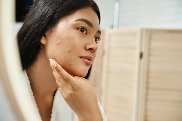 Junge asiatische Frau mit brünetten Haaren und zu Akne neigender Haut beim Anblick des Spiegels im Badezimmer, Banner — Stockfoto