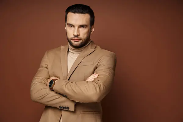 Handsome man in turtleneck and blazer giving confident look while standing with folded arms on beige — Stock Photo