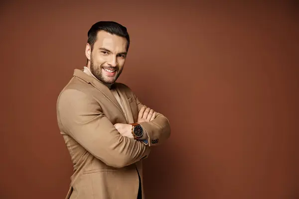 Cheerful man with bristle posing in stylish beige blazer with folded arms on beige backdrop — Stock Photo