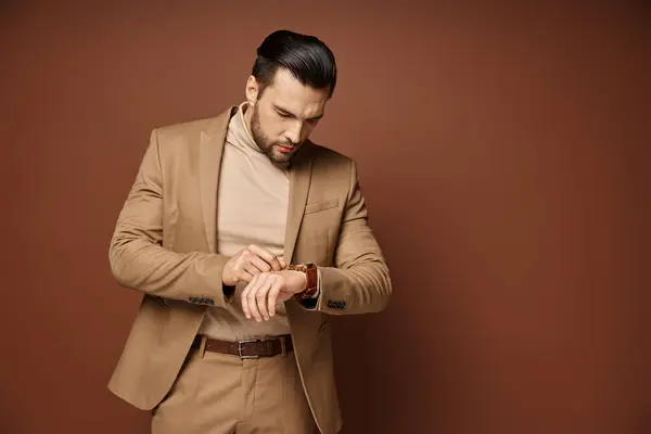 Homem bonito em traje elegante olhando para o seu relógio de pulso em fundo bege, gerenciamento de tempo — Fotografia de Stock