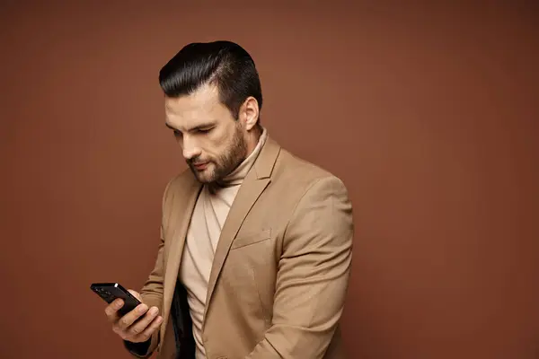 Handsome businessman in elegant attire checking his smartphone on beige background, networking — Stock Photo