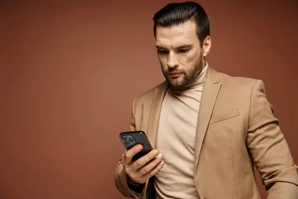 Handsome businessman in elegant attire checking his smartphone on beige background, connected — Stock Photo
