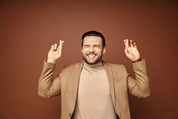 Portrait of attractive man in elegant attire smiling with his fingers crossed on beige background — Stock Photo