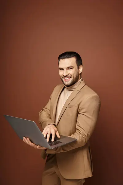 Alegre y guapo profesional usando su portátil mientras trabaja remotamente sobre fondo beige - foto de stock