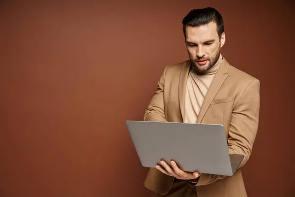 Profesional enfocado y guapo usando su computadora portátil mientras trabaja remotamente sobre fondo beige - foto de stock