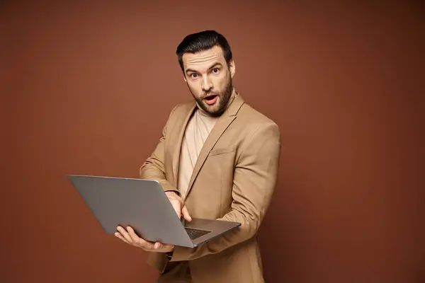 Шокированный и красивый профессионал, использующий свой ноутбук, работая скромно на бежевом фоне — стоковое фото