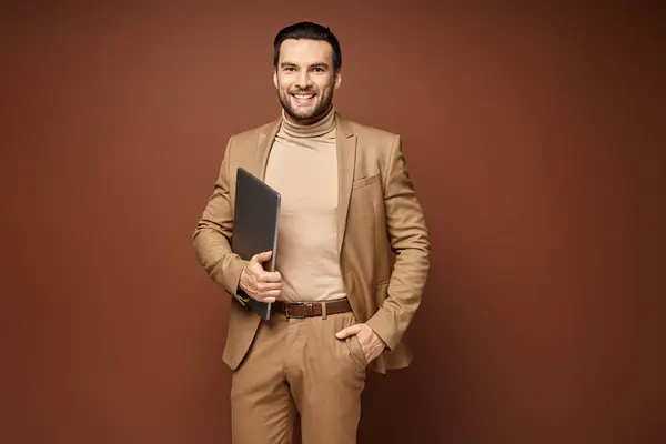 Happy businessman in elegant attire standing with his laptop on beige background, remote work — Stock Photo