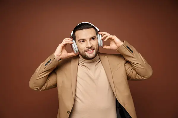 Charismatischer Mann in eleganter Kleidung genießt Musik in seinen drahtlosen Kopfhörern auf beigem Hintergrund — Stockfoto