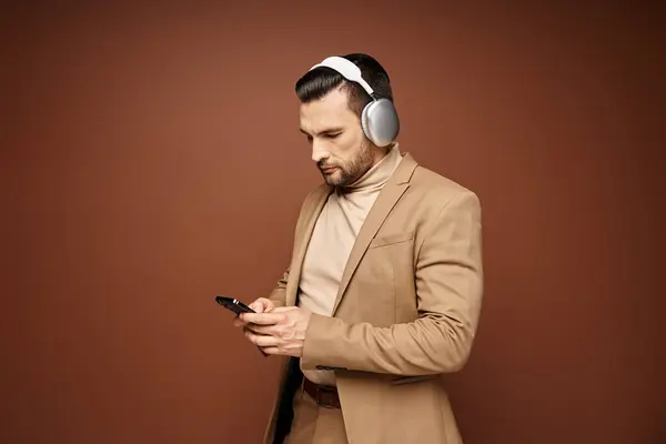 Schöner Mann in eleganter Kleidung mit Smartphone und Kopfhörer, beiger Hintergrund — Stockfoto