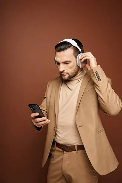 Homem bonito em fones de ouvido sem fio usando seu smartphone em fundo bege, era digital — Fotografia de Stock