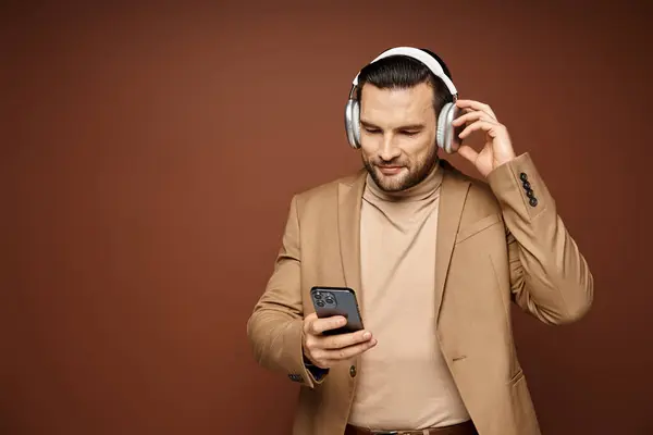 Smiling handsome man in wireless headphones using his smartphone on beige background, digital age — Stock Photo