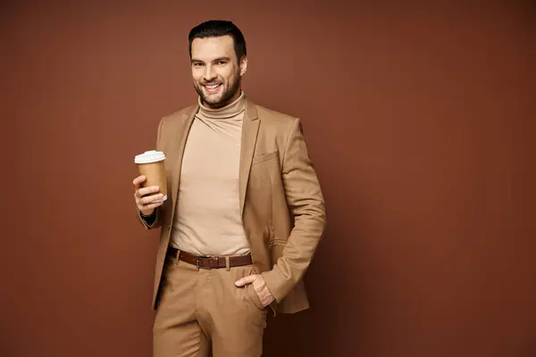 Homme heureux en tenue élégante tenant café pour aller et debout avec la main dans la poche sur fond beige — Photo de stock