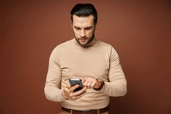 Handsome man with bristle in turtleneck using his smartphone on beige background, social media — Stock Photo