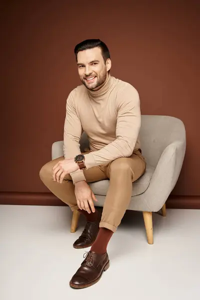 Uomo allegro e bello in dolcevita seduto su una comoda poltrona su sfondo beige — Foto stock