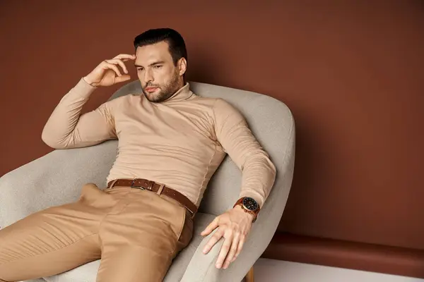 Pensive man in turtleneck sitting on comfortable armchair and looking away on beige backdrop — Stock Photo