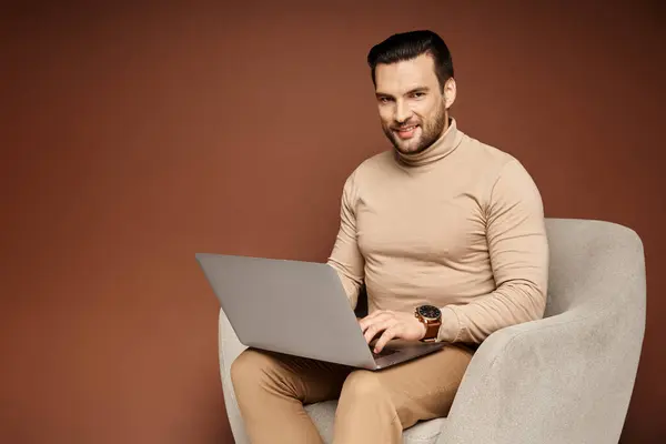 Glücklicher Mann im Rollkragen sitzt auf bequemen Sesseln und benutzt Laptop auf beigem Hintergrund — Stockfoto