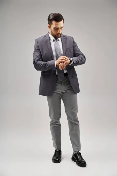 Bel homme d'affaires posant dans un costume élégant vérifiant sa montre sur fond gris, élégance — Photo de stock