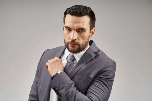 Intense gaze from a handsome man with bristle posing in a grey suit on light background in studio — Stock Photo
