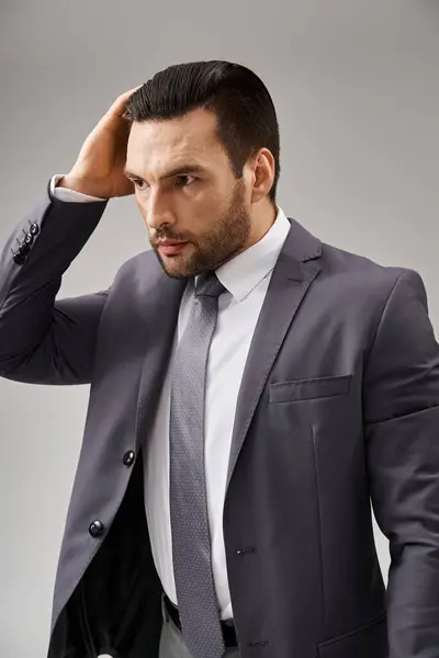 Bell'uomo in abito formale con cravatta che regola i capelli su sfondo grigio, moda aziendale — Foto stock