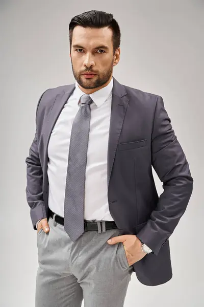 Charismatic businessman in suit posing with confident stance and looking at camera on grey backdrop — Stock Photo