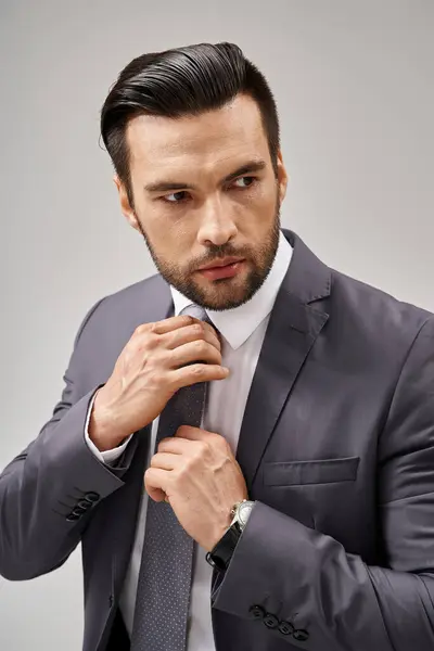 Hombre guapo en ropa formal ajustando su corbata sobre fondo gris, moda corporativa - foto de stock