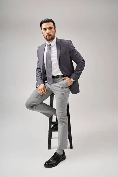 Handsome businessman with bristle posing with hand in pocket in suit and sitting on high stool — Stock Photo