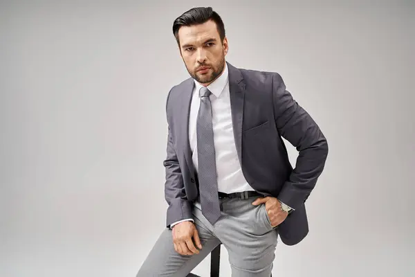Handsome businessman with bristle posing with hand in pocket in suit and sitting on high stool — Stock Photo