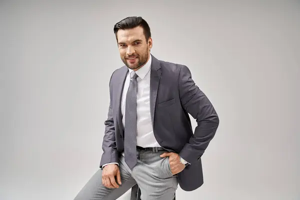 Happy businessman with bristle posing with hand in pocket in suit and sitting on high stool — Stock Photo
