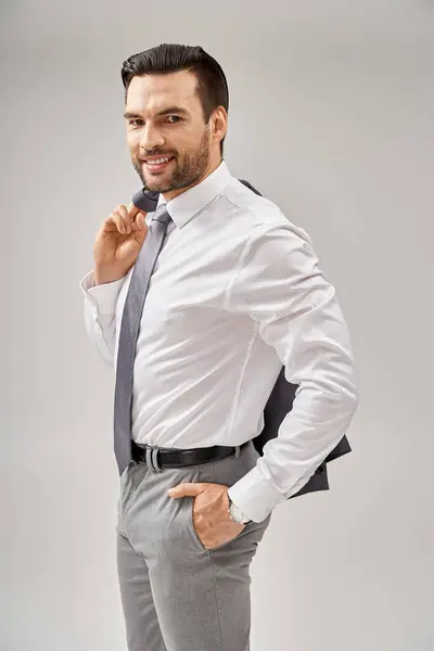 Hombre de negocios sonriente con cerdas sosteniendo la chaqueta sobre el hombro mientras está de pie con la mano en el bolsillo - foto de stock