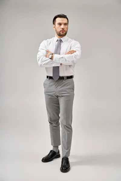 Full length of businessman in suit standing with crossed arms while posing on grey background — Stock Photo