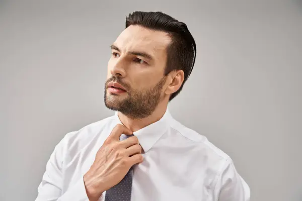 Portrait of handsome businessman in white shirt adjusting tie on grey background, elegant attire — Stock Photo