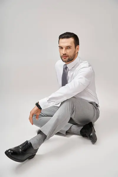 Handsome businessman in elegant formal wear sitting on floor in studio with grey background — Stock Photo