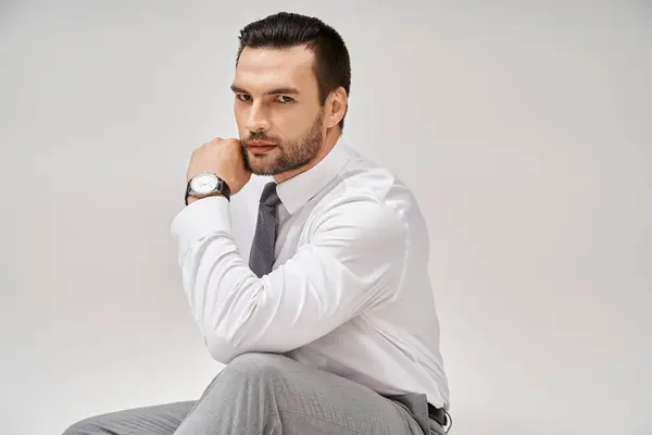 Good looking businessman in elegant formal wear sitting on floor in studio with grey background — Stock Photo