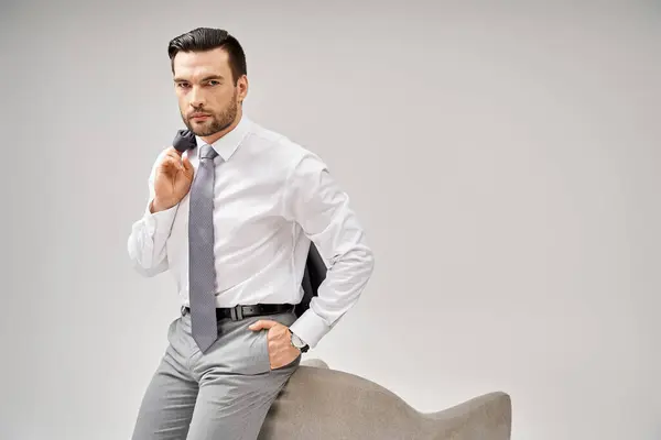Élégant homme d'affaires en costume posant avec la main dans la poche et appuyé sur un fauteuil sur fond gris — Photo de stock