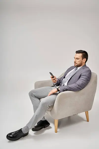 Relaxed businessman sitting on armchair and using smartphone on grey background, social media — Stock Photo