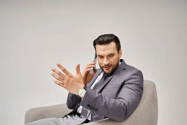Geschäftsmann mit Borsten auf Sessel sitzend und Smartphone auf grauem Hintergrund — Stockfoto