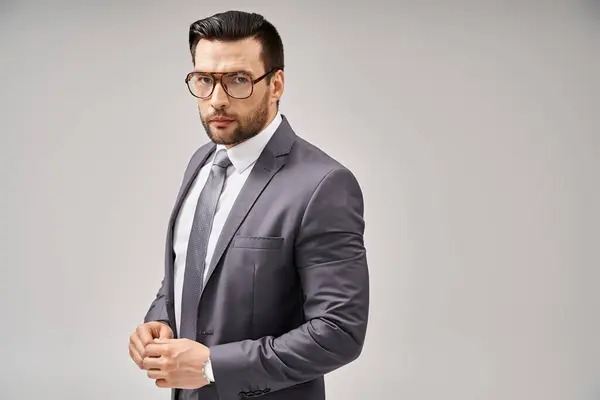 Handsome businessman in formal wear and glasses standing on grey background, elegance and style — Stock Photo