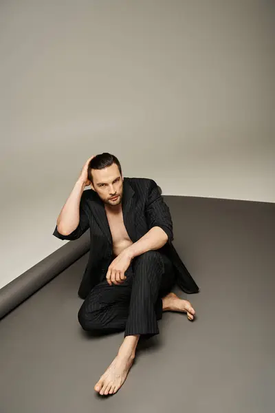 Stylischer und gutaussehender Mann mit nackter Brust und Füßen posiert im Nadelstreifenanzug auf grauem Hintergrund — Stockfoto