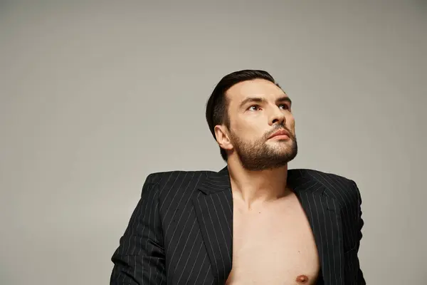 Porträt eines eleganten und gut aussehenden Mannes mit nackter Brust, der im Nadelstreifenanzug auf grauem Hintergrund posiert — Stockfoto