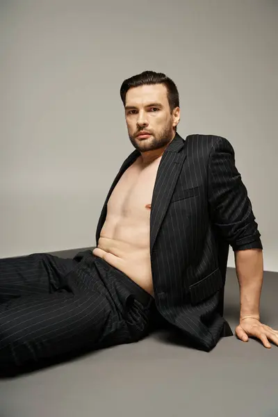 Портрет стильного і красивого чоловіка з голими грудьми, що позує в одязі зі стрічкою на сірому фоні — стокове фото